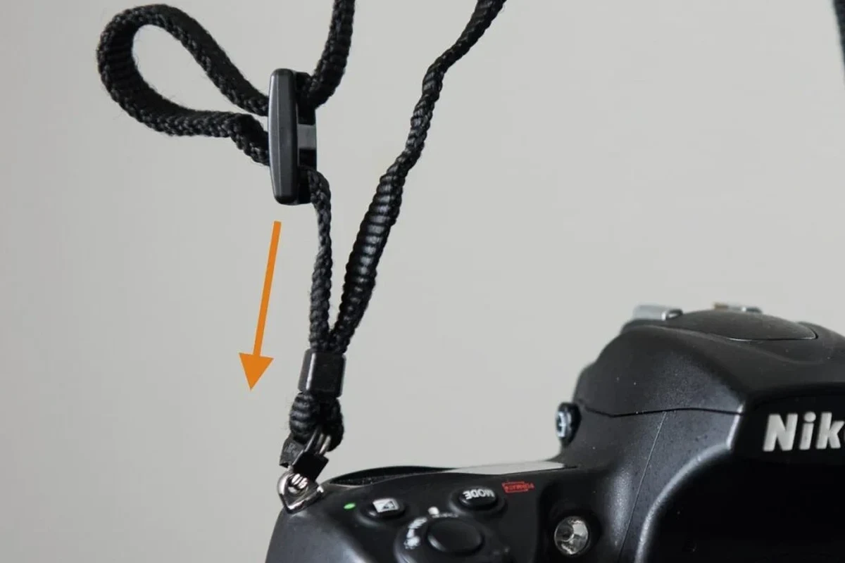 Camera strap being attached to a mirrorless camera body on a clean tabletop