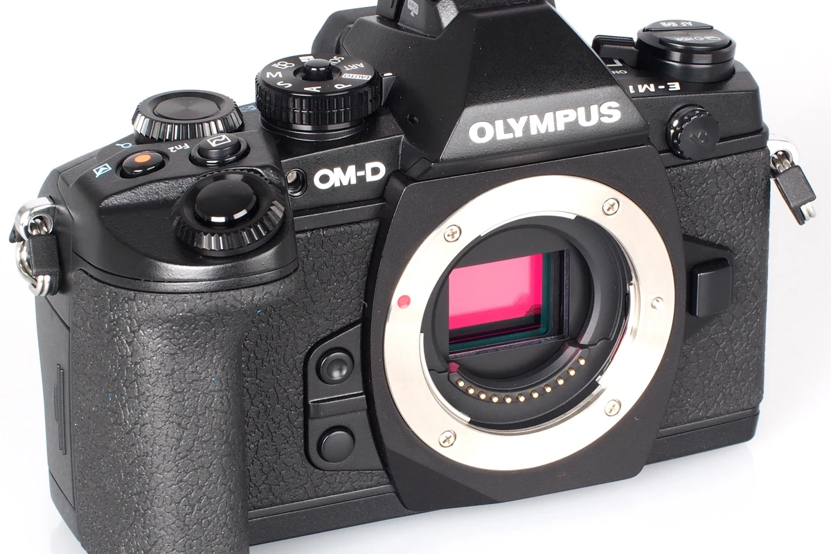 Compact Omd Em1 camera with attached lens on a desk beside memory cards and camera strap