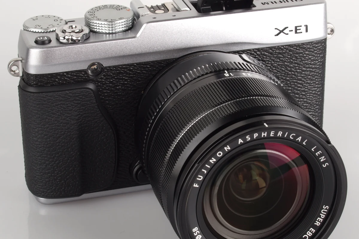 Compact Fujifilm X-E1 mirrorless camera body on a desk with a lens and memory card