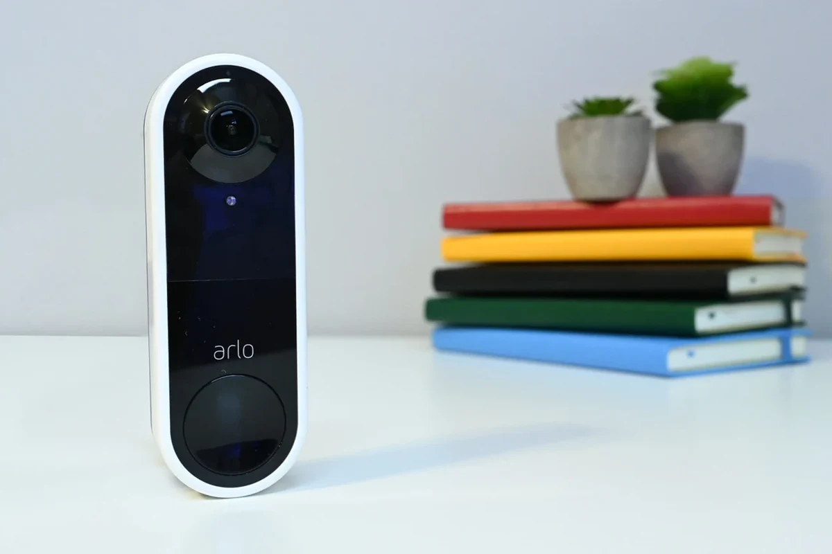 Arlo video doorbell mounted beside a front door with Apple Home app integration on a smartphone