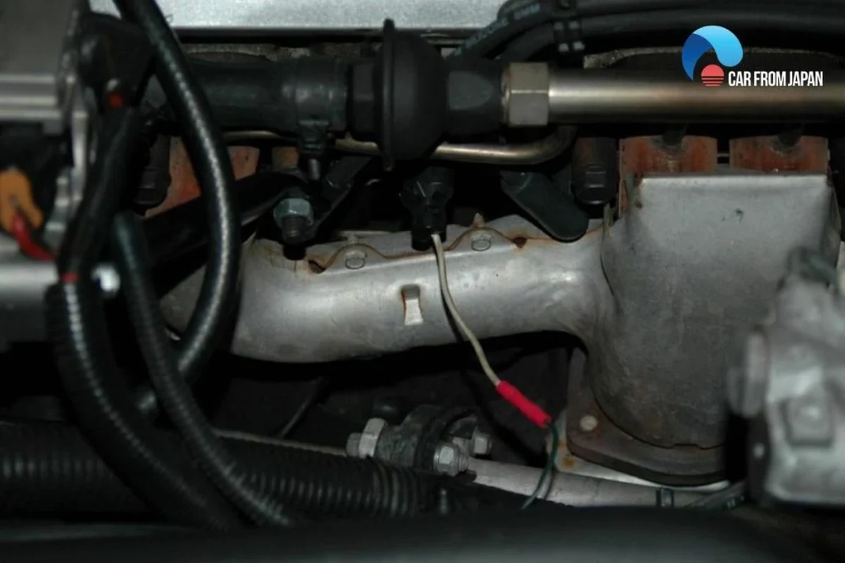 Mechanic inspecting engine sensor wiring near a car engine block for misfire diagnosis