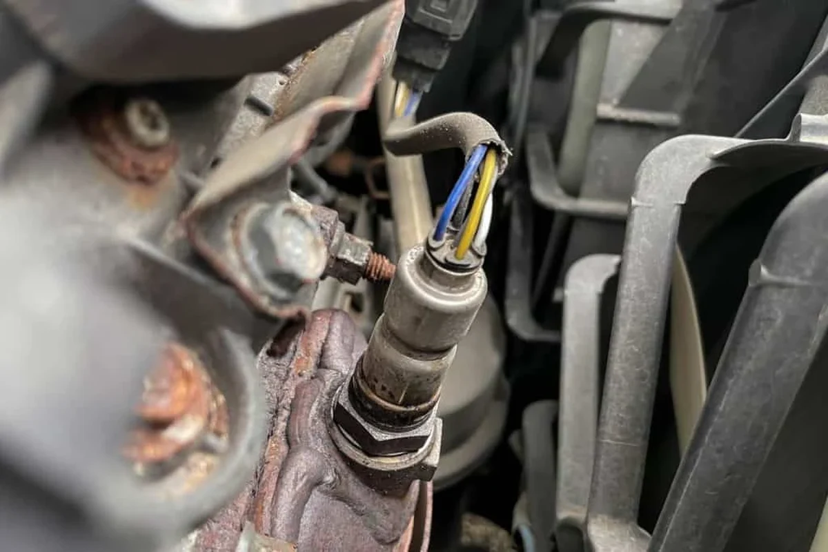 Mechanic replacing an oxygen sensor on a car exhaust system with basic hand tools